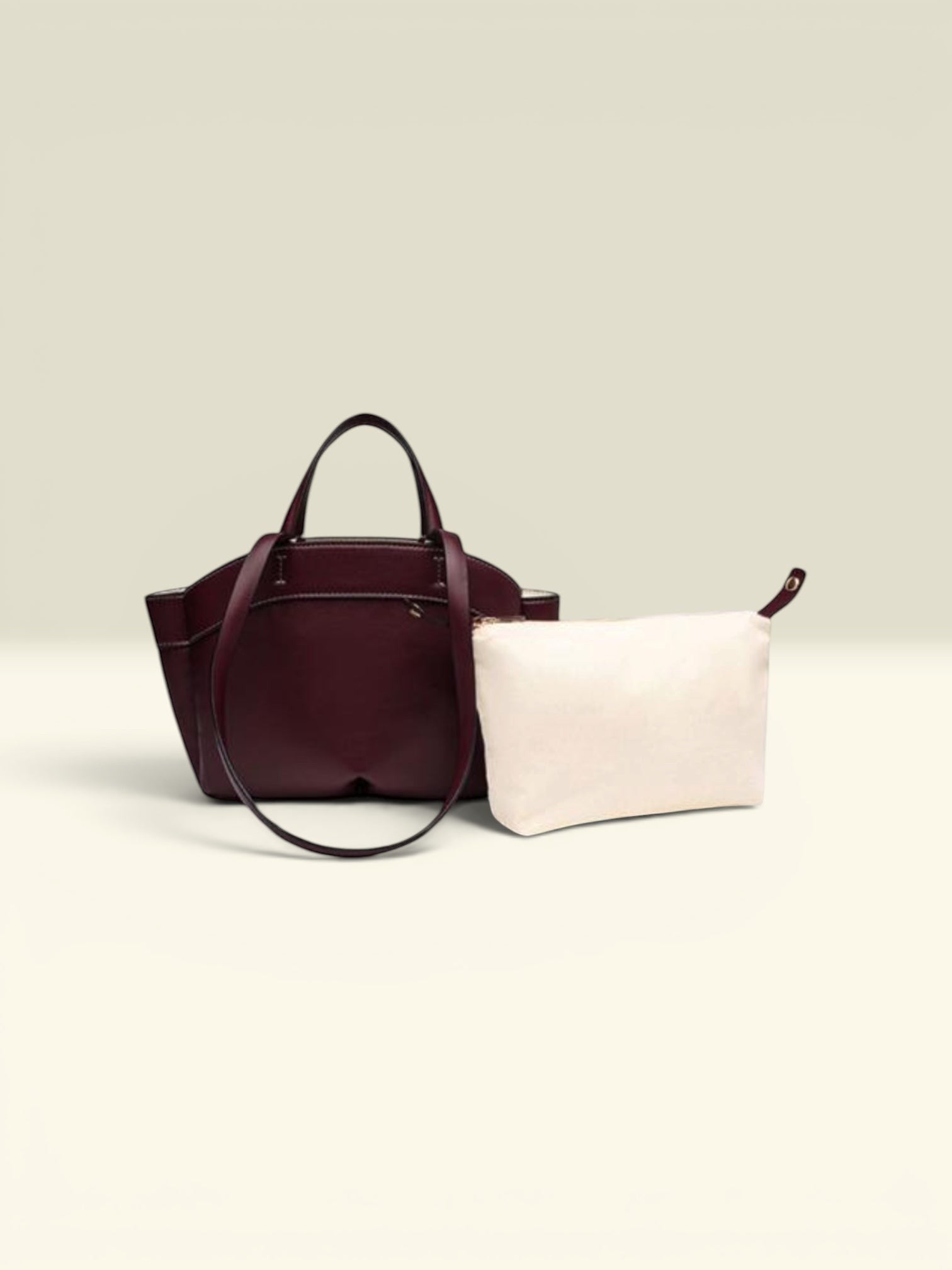THE GOOD FIND burgundy leather tote bag with matching cream pouch. Features top handles and a sleek design.