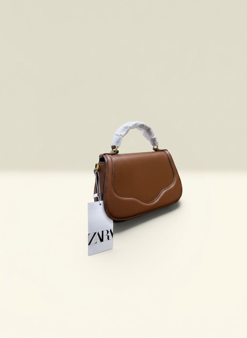 THE GOOD FIND sculpted top handle bag in cognac faux leather with a unique flap and gold hardware.